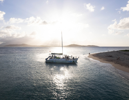 Sailboat near sandy shore at sunset with distant mountains.