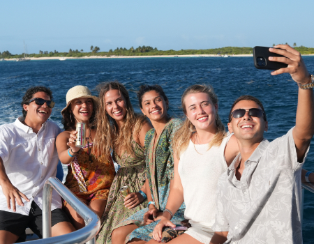 Group of friends taking a selfie on a boat with ocean in background.