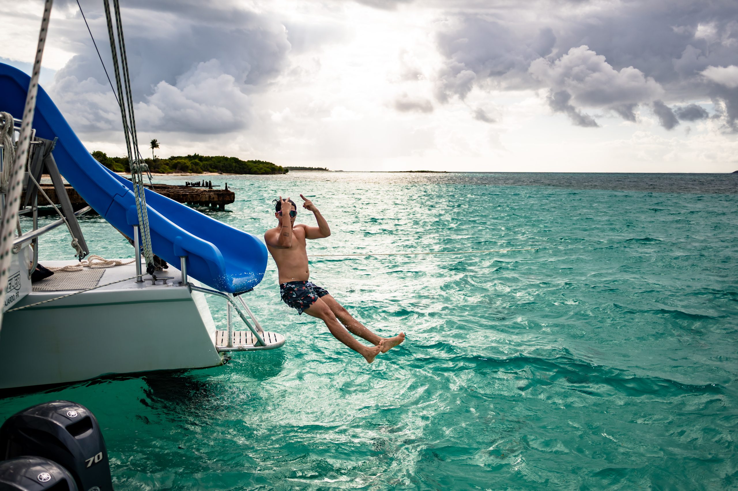 Person sliding off boat into turquoise sea near tropical island.