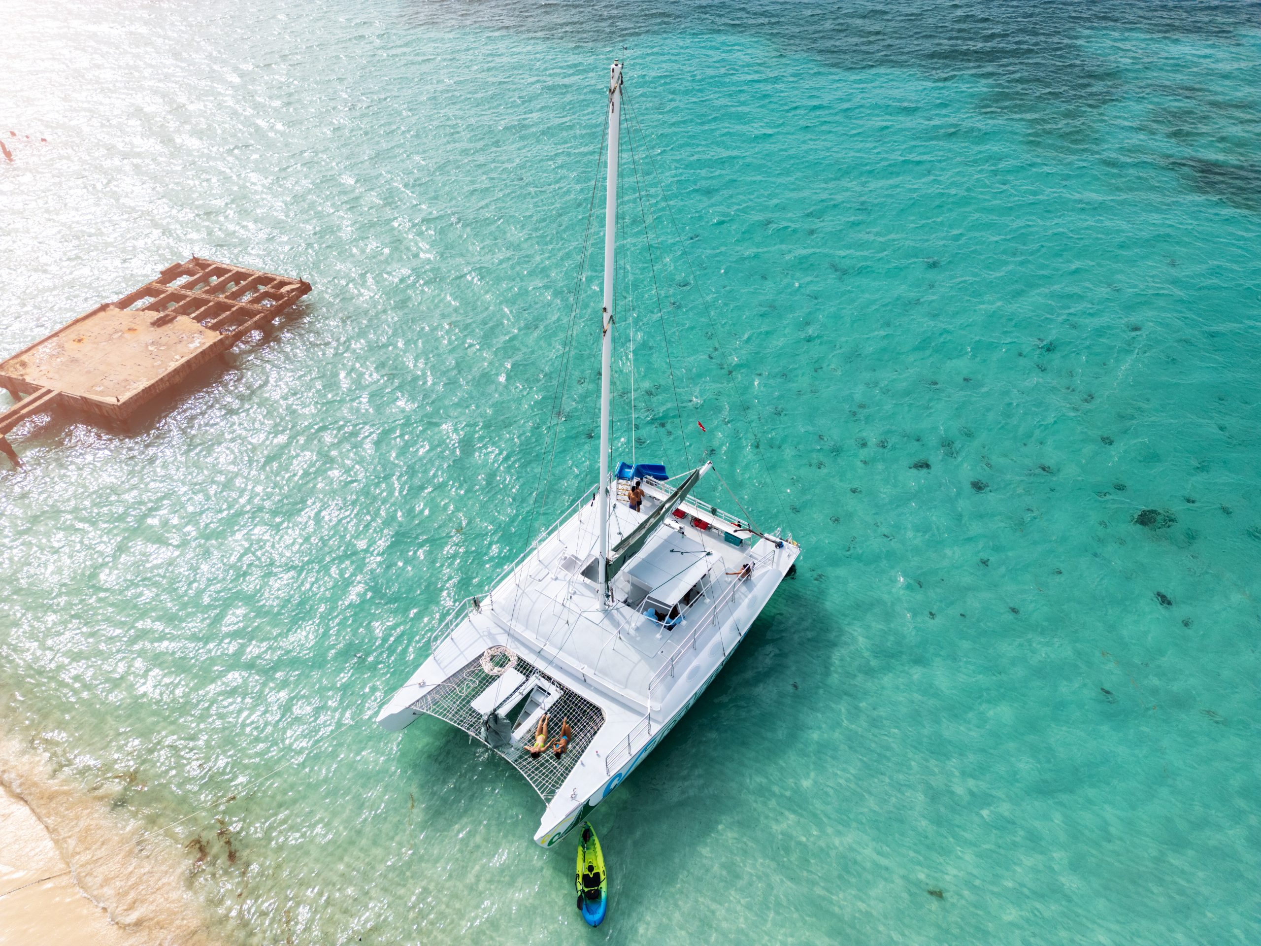 Catamaran in turquoise water near a sandy beach.