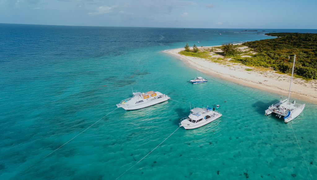 Three catamarans anchored near a sandy beach with clear turquoise waters and green vegetation.
